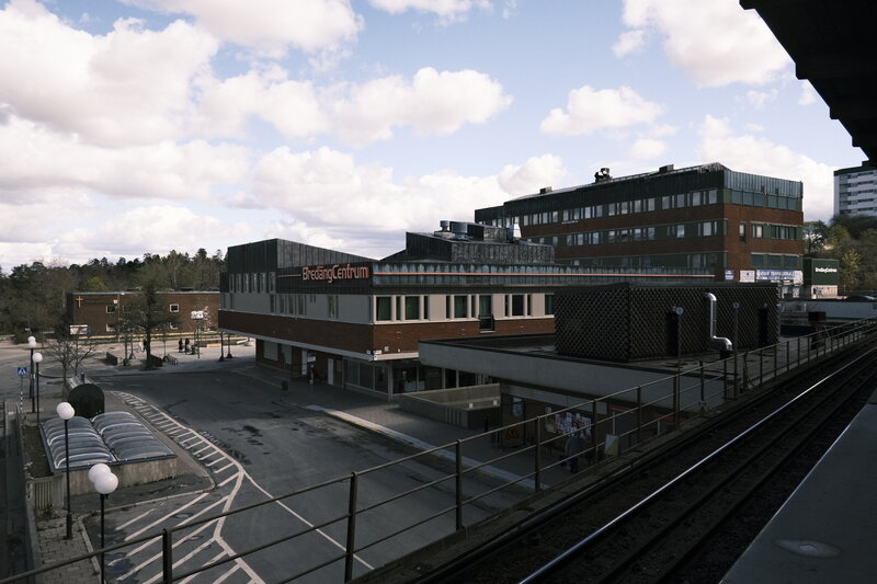 Wide view of Bredäng Centrum and surrounding streets from an elevated metro platform, blue sky with scattered clouds